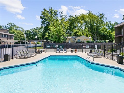 A large swimming pool surrounded by a fence and lounge chairs.