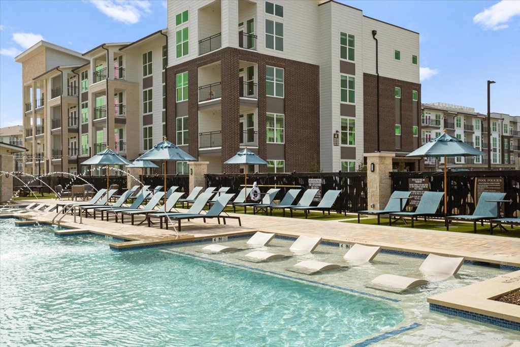 a swimming pool with lounge chairs in front of an apartment building
