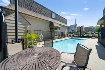A patio with a table and chairs overlooking a pool. at Malvern Hill Apartment Homes, 66103