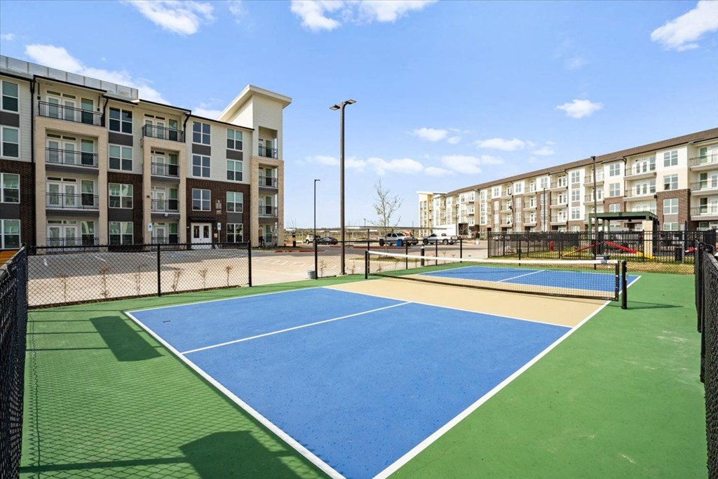 an outdoor tennis court with apartments in the background