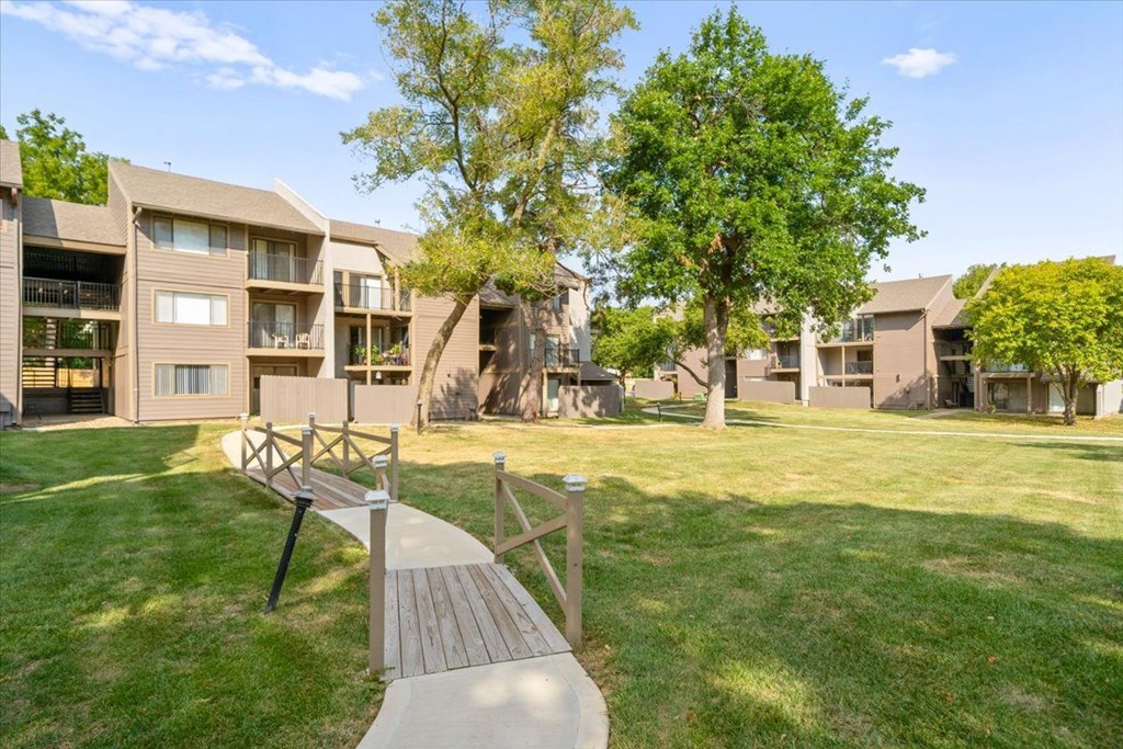 A wooden walkway leads to a grassy area in front of apartment buildings.