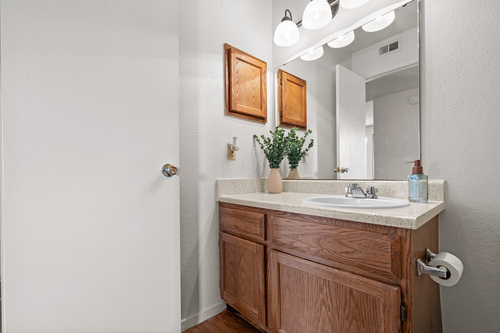A bathroom with a wooden vanity and a mirror. at Coventry Oaks Apartments, Kansas