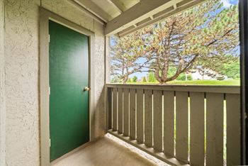 A green door is on the left of a balcony with a view of trees. at Coventry Oaks Apartments, Overland Park, KS, 66214