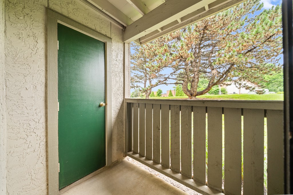 A green door is on the left of a balcony with a view of trees. at Coventry Oaks Apartments, Kansas, 66214