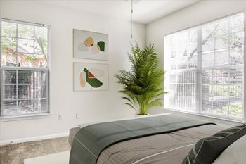 A bedroom with a bed, a plant, and two framed pictures on the wall. at Wynnewood Farms Apartments, Overland Park, Kansas