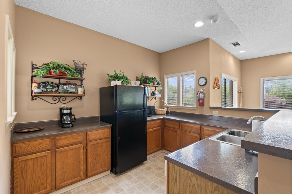 A kitchen with a black refrigerator and wooden cabinets at Coventry Oaks Apartments, Overland Park, KS