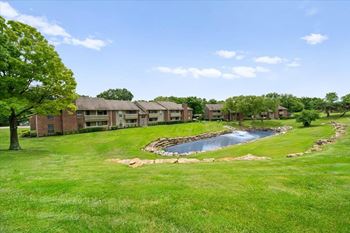 A small pond in the middle of a grassy area with a building in the background. at Coventry Oaks Apartments, Kansas