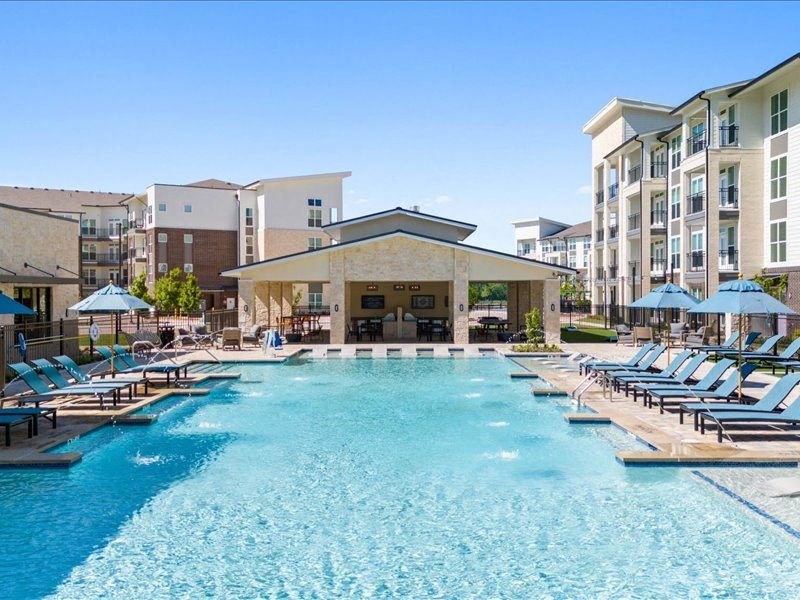 an outdoor pool with lounge chairs and an apartment building
