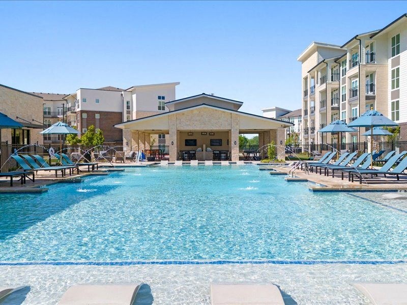 a large swimming pool with lounge chairs and an apartment building