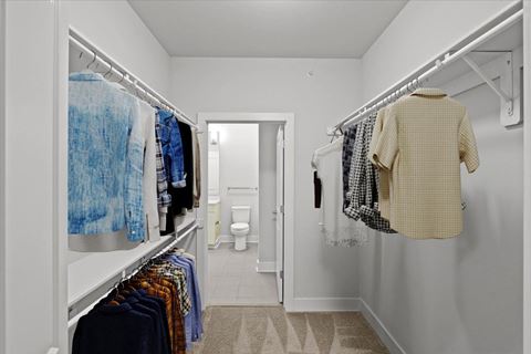 a long white closet with clothes hanging in it and a white bathroom