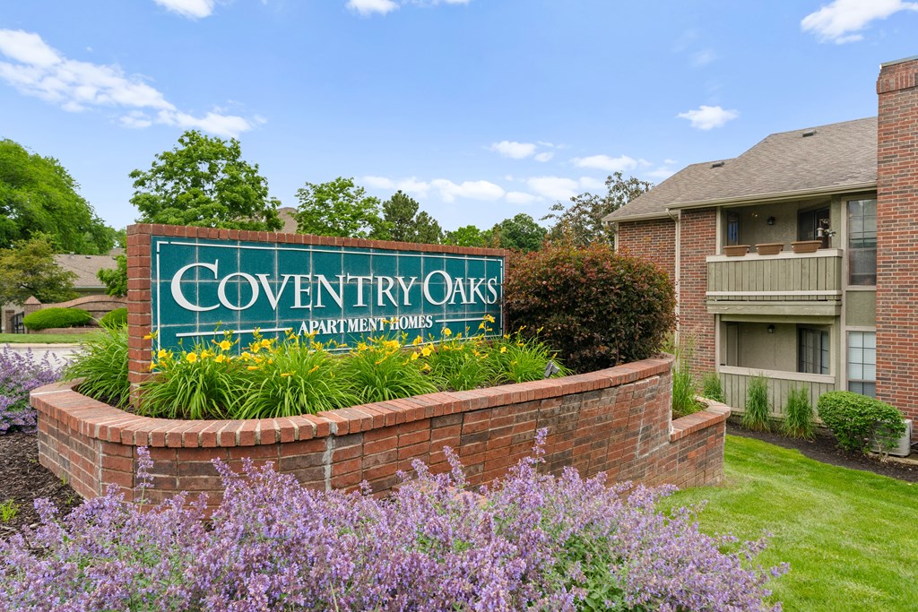 A sign for Coventry Oaks Apartment Homes is surrounded by flowers and greenery. at Coventry Oaks Apartments, Overland Park, Kansas