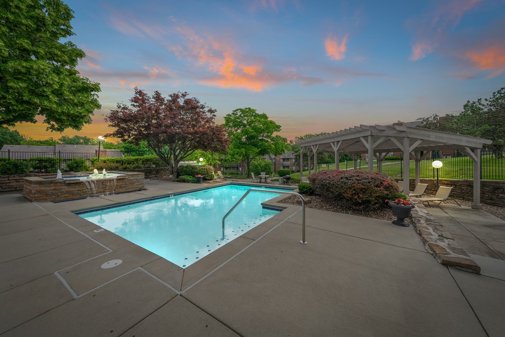 A swimming pool surrounded by a concrete patio and a stone wall with a fountain. at Coventry Oaks Apartments, Kansas