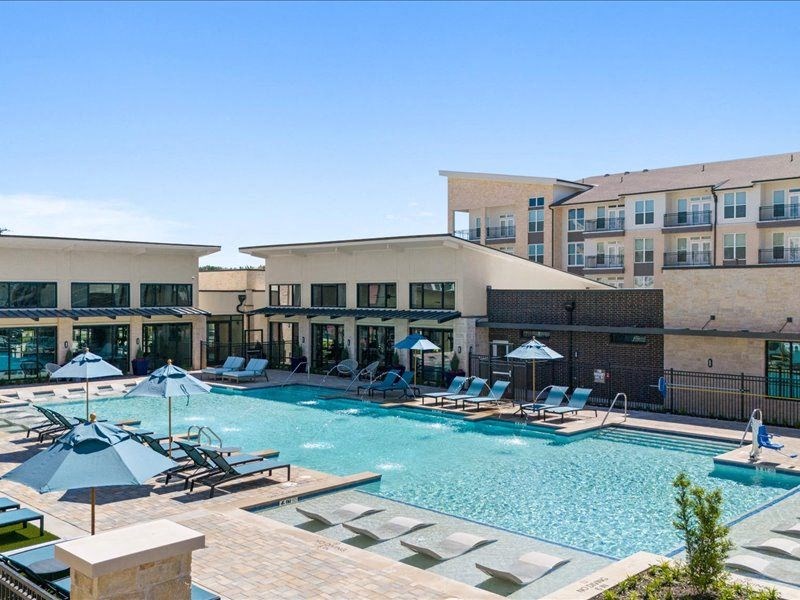 a large swimming pool with chairs and umbrellas in front of a building