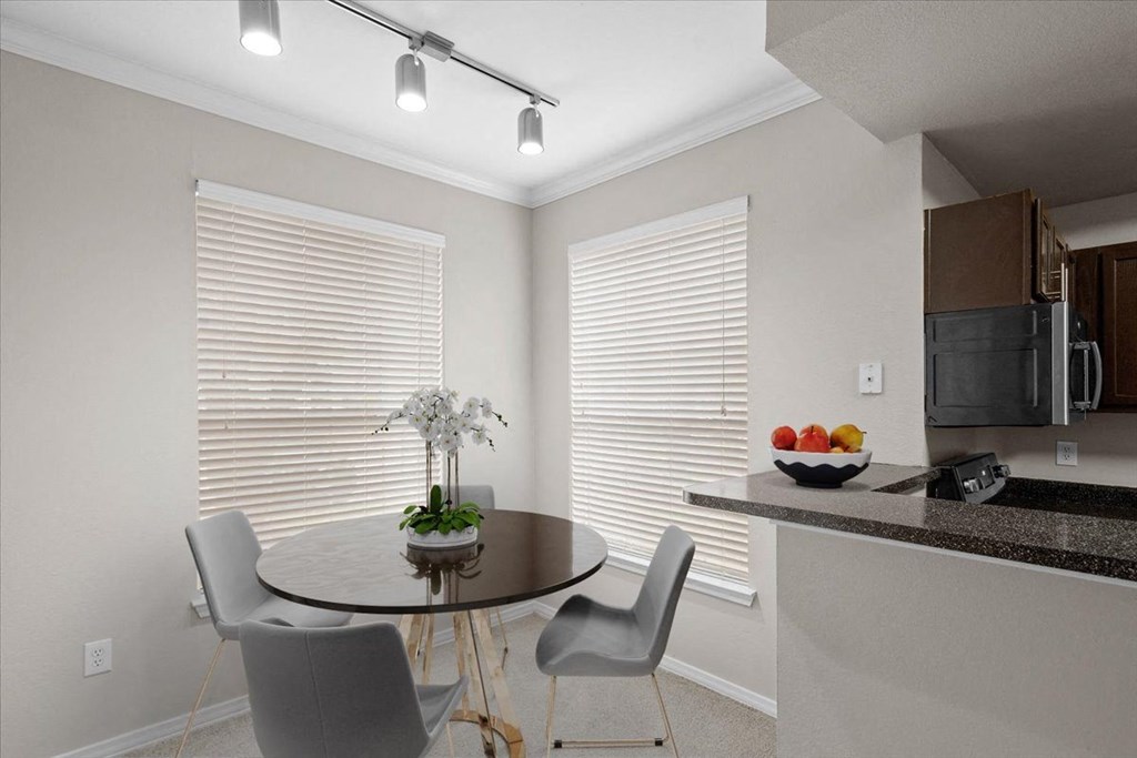 a dining area with a table and chairs and a kitchen in the background at The Clairborne Apartment Homes, Grand Prairie, TX