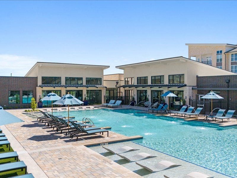 a swimming pool with chairs and umbrellas in front of a building