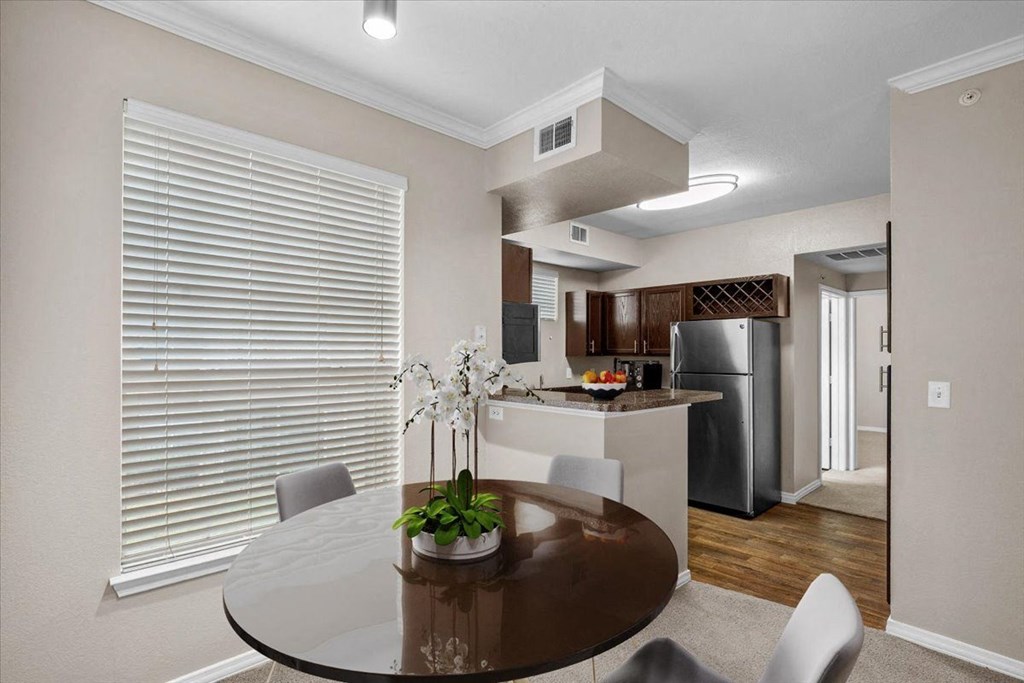 a dining area with a table and chairs and a kitchen in the background at The Clairborne Apartment Homes, Grand Prairie, TX