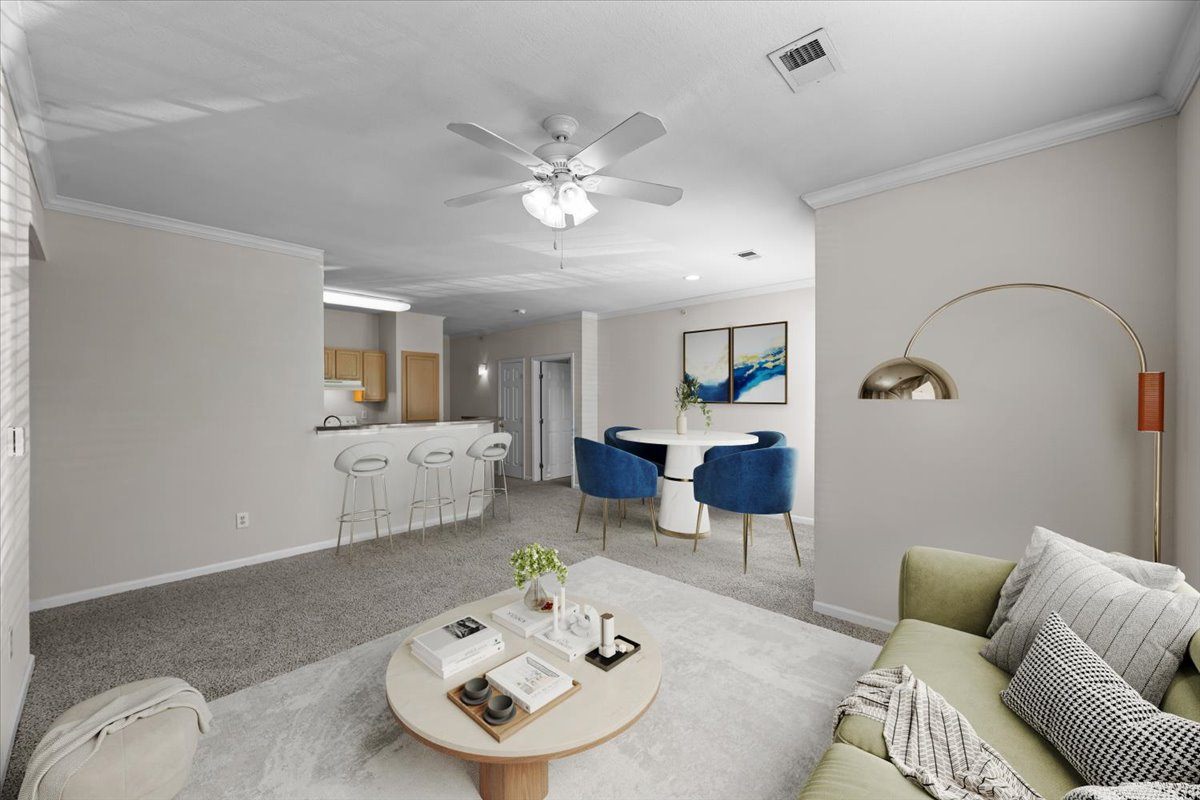 A living room with a grey carpet and a white ceiling fan.