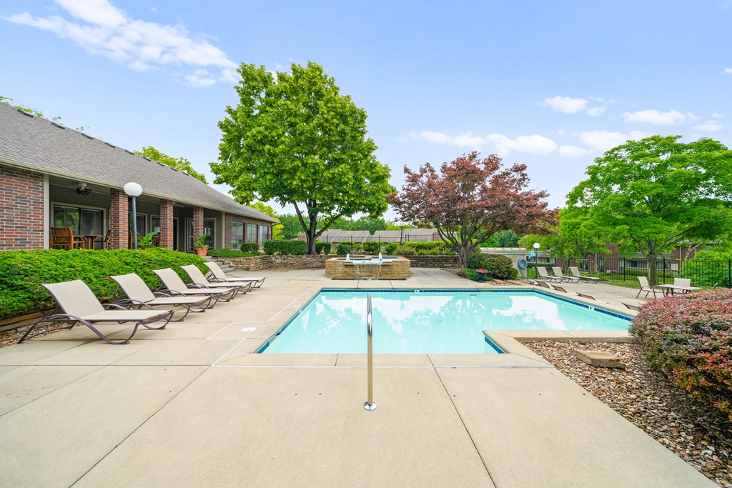 A pool surrounded by trees and chairs in front of a house. at Coventry Oaks Apartments, Overland Park