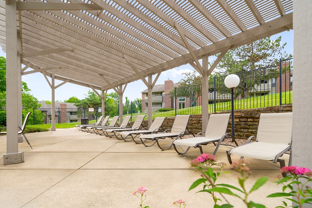 A row of lounge chairs are set up under a white pergola. at Coventry Oaks Apartments, Kansas