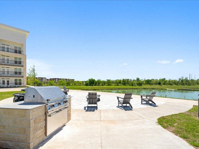 a patio with a grill and chairs near a body of water