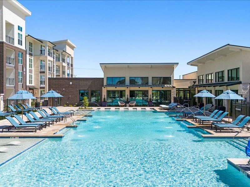 a large swimming pool with lounge chairs and umbrellas in front of a building