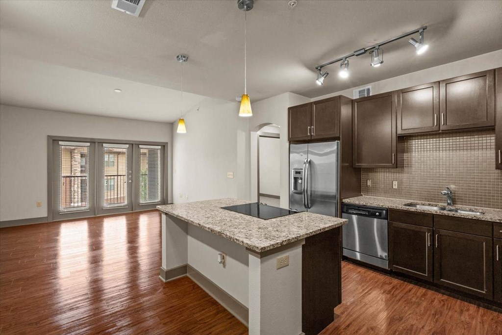 a kitchen with a large island with granite countertops and dark wood cabinets at Cypress at Lewisville Apartment Homes, Texas