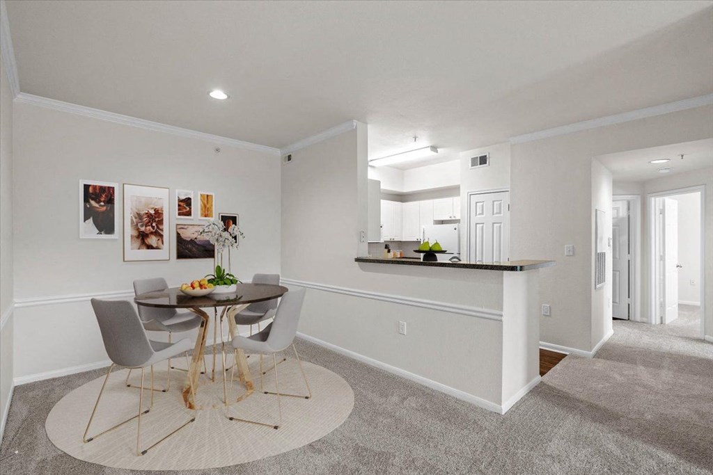 a dining area with a small table and chairs and a kitchen in the background