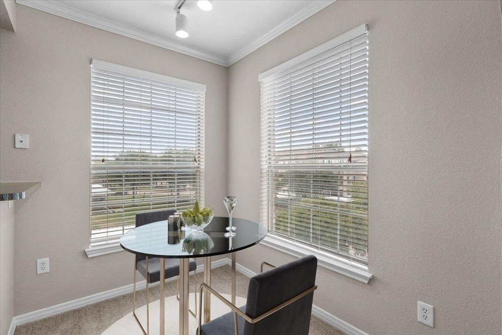 a dining room with two windows and a table with two chairs at The Clairborne Apartment Homes, Grand Prairie, Texas