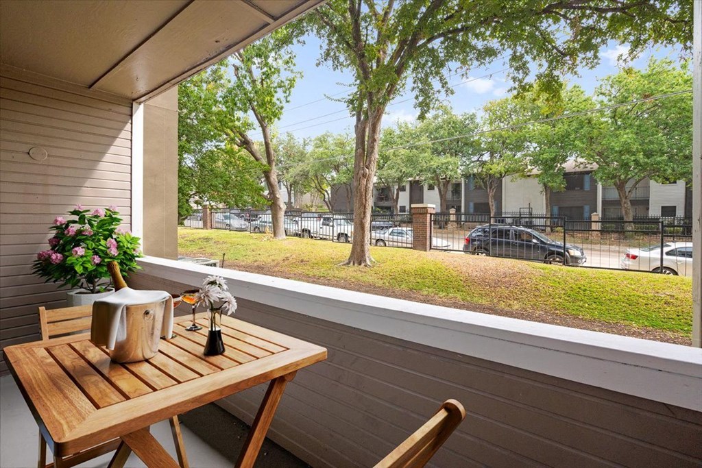 a balcony with a wooden table and two chairs and a large window with a view of a at Creekview Apartment Homes, Dallas, 75254