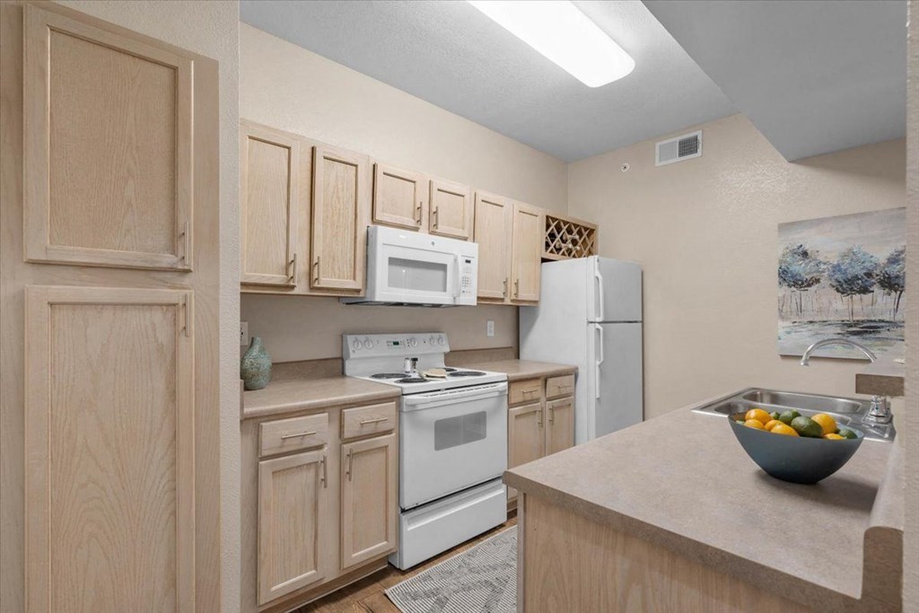 a kitchen with white appliances and wooden cabinets at The Clairborne Apartment Homes, Grand Prairie