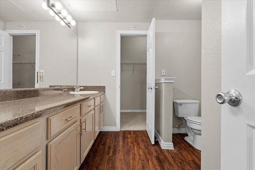 a bathroom with a toilet sink and mirror at The Clairborne Apartment Homes, Grand Prairie, TX