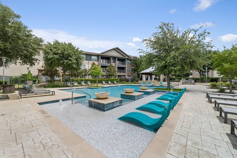A large outdoor swimming pool with loungers and a building in the background.