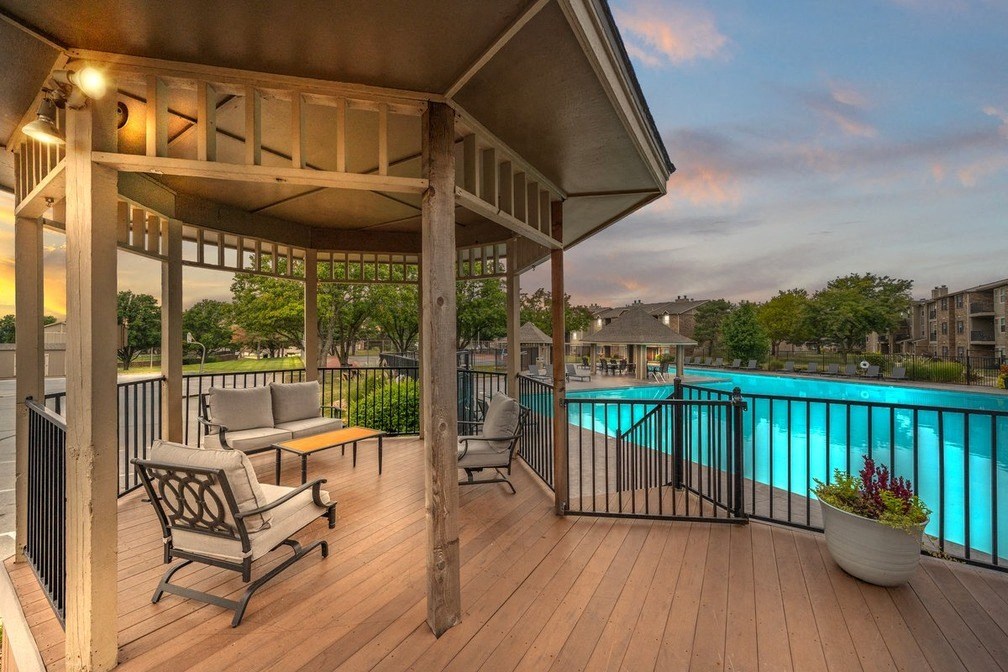 a poolside deck with chairs and a gazebo overlooking a swimming pool
