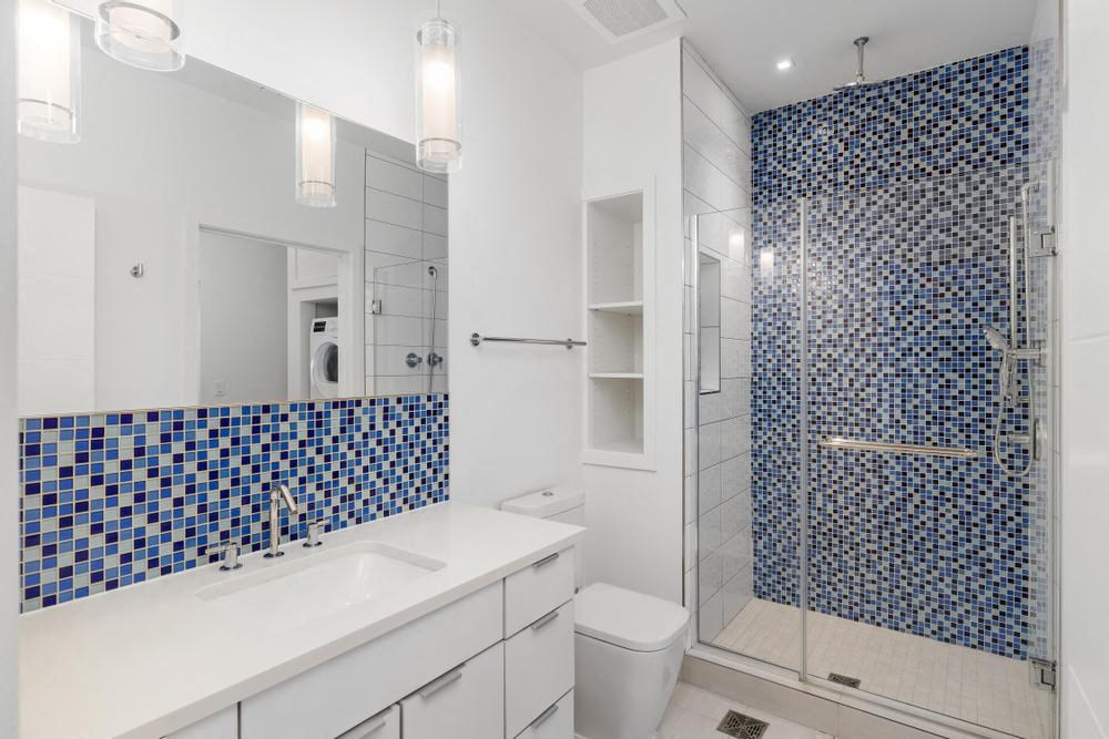 A bathroom with a blue tiled shower and white countertop at Sky On Main Apartments, Missouri City 64105