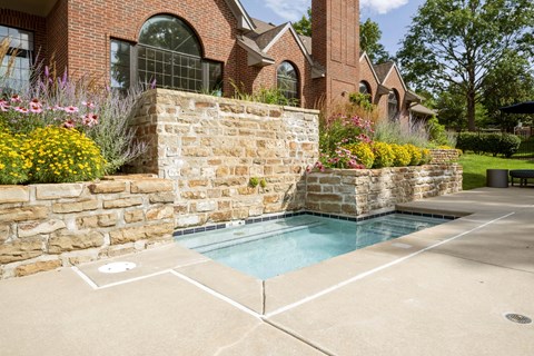 Shallow kiddie pool with stone landscaping and flower beds beside the community pool area.