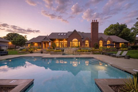 Twilight view of the community pool and clubhouse with illuminated windows and landscaped grounds.
