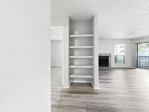 A white bookshelf with several shelves is in a room with a wooden floor and a window.