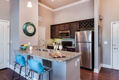 A kitchen with a granite countertop and a stainless steel refrigerator.