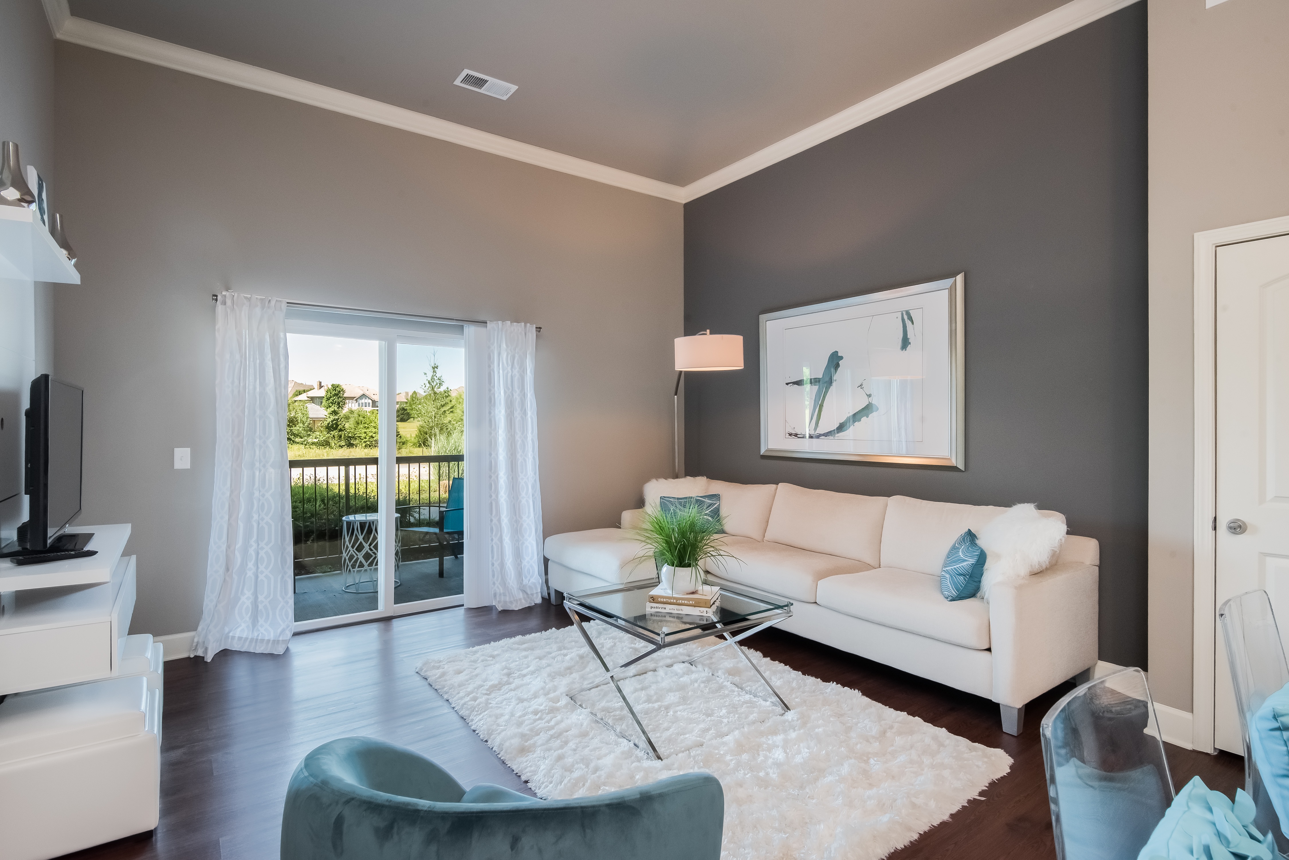 A living room with a white couch, a glass coffee table, and a painting on the wall.