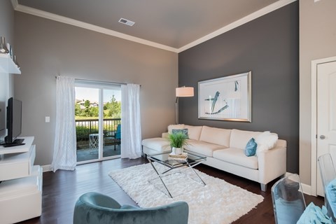 A living room with a white couch, a glass coffee table, and a painting on the wall.