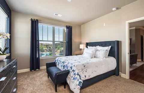 A bedroom with a large bed and a window with blue curtains.