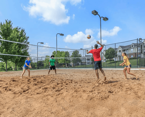 Four people playing volleyball on a sandy court.