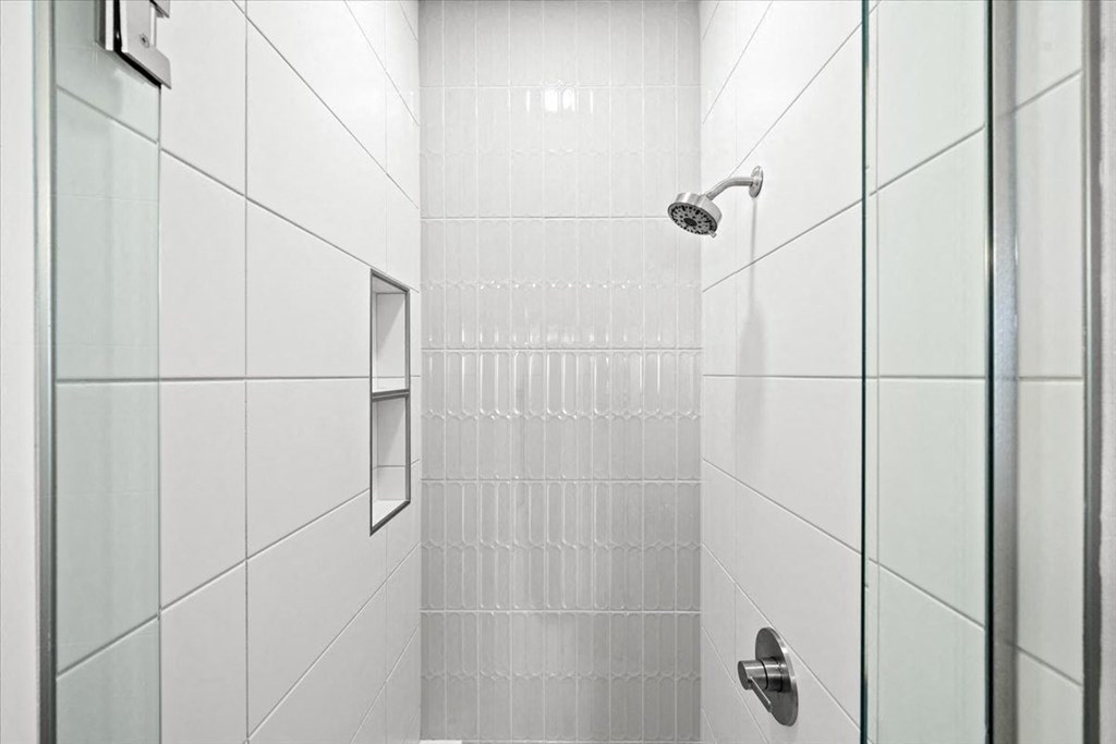 A white tiled shower with a glass door and a silver handle at Sky On Main Apartments, Missouri