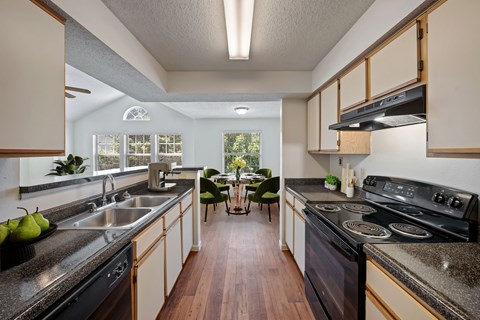 Apartment kitchen with black appliances, double sink, and open dining area at Stonebriar Apartments