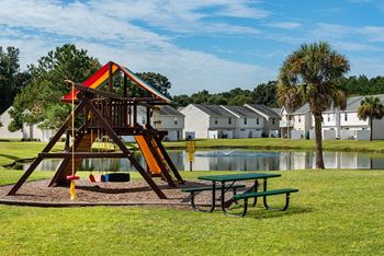 a swing set with a picnic table in a park next to a lake