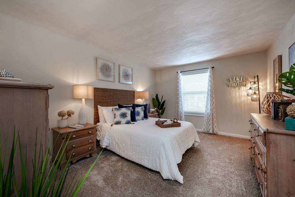 A bedroom with a bed, nightstand, and a window with white curtains.