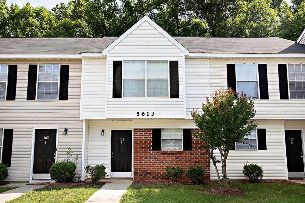 A white house with black shutters and a brick wall in front.