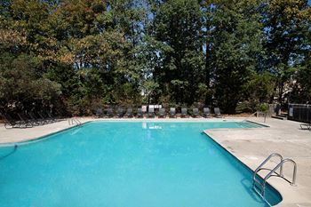 a swimming pool with chaise lounge chairs and trees in the background