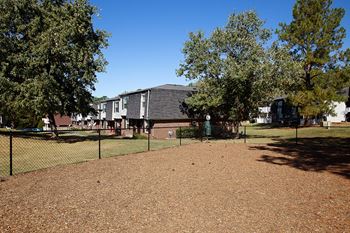 A field with a fence and trees with buildings in the background.