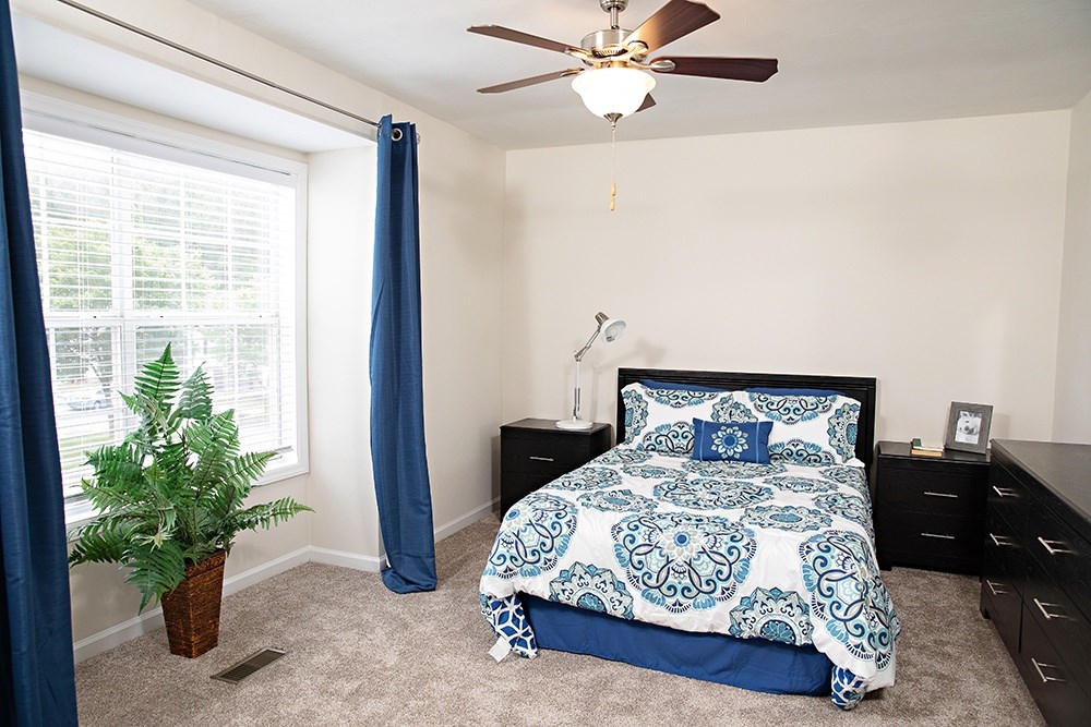 A bedroom with a bed, dresser, and ceiling fan.
